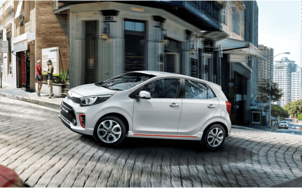 A white color picanto car driving a small hill in a city